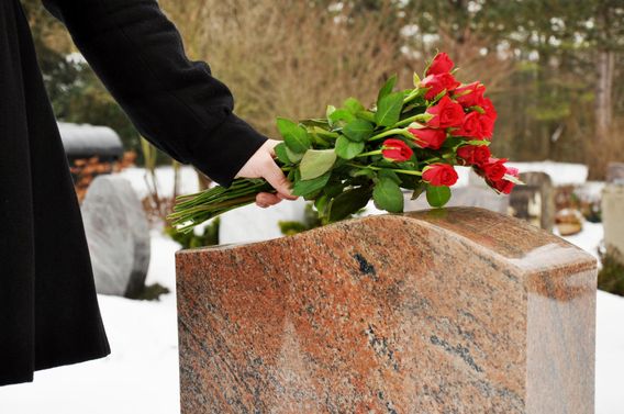 Person hält Strauß mit roten Rosen an braunen Marmor-Grabstein